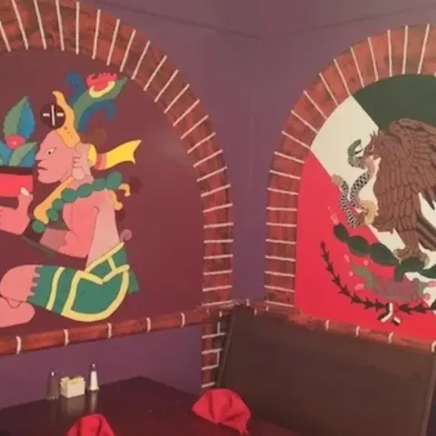 Brick arches on a purple dining room wall, painted with an Aztec figure and the eagle from the Mexican flag