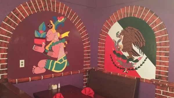 Brick arches on a purple dining room wall, painted with an Aztec figure and the eagle from the Mexican flag